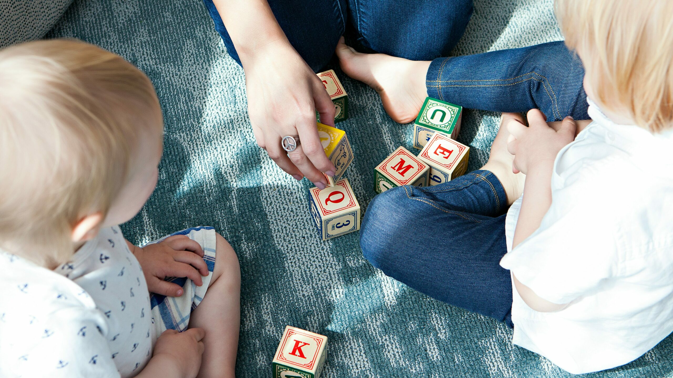 Two children engage with educational wooden blocks under the guidance of an adult, illustrating a screen-free learning environment. This scene contrasts with the effects of kids' screen time, emphasizing the importance of hands-on educational activities and direct interaction in early childhood development.