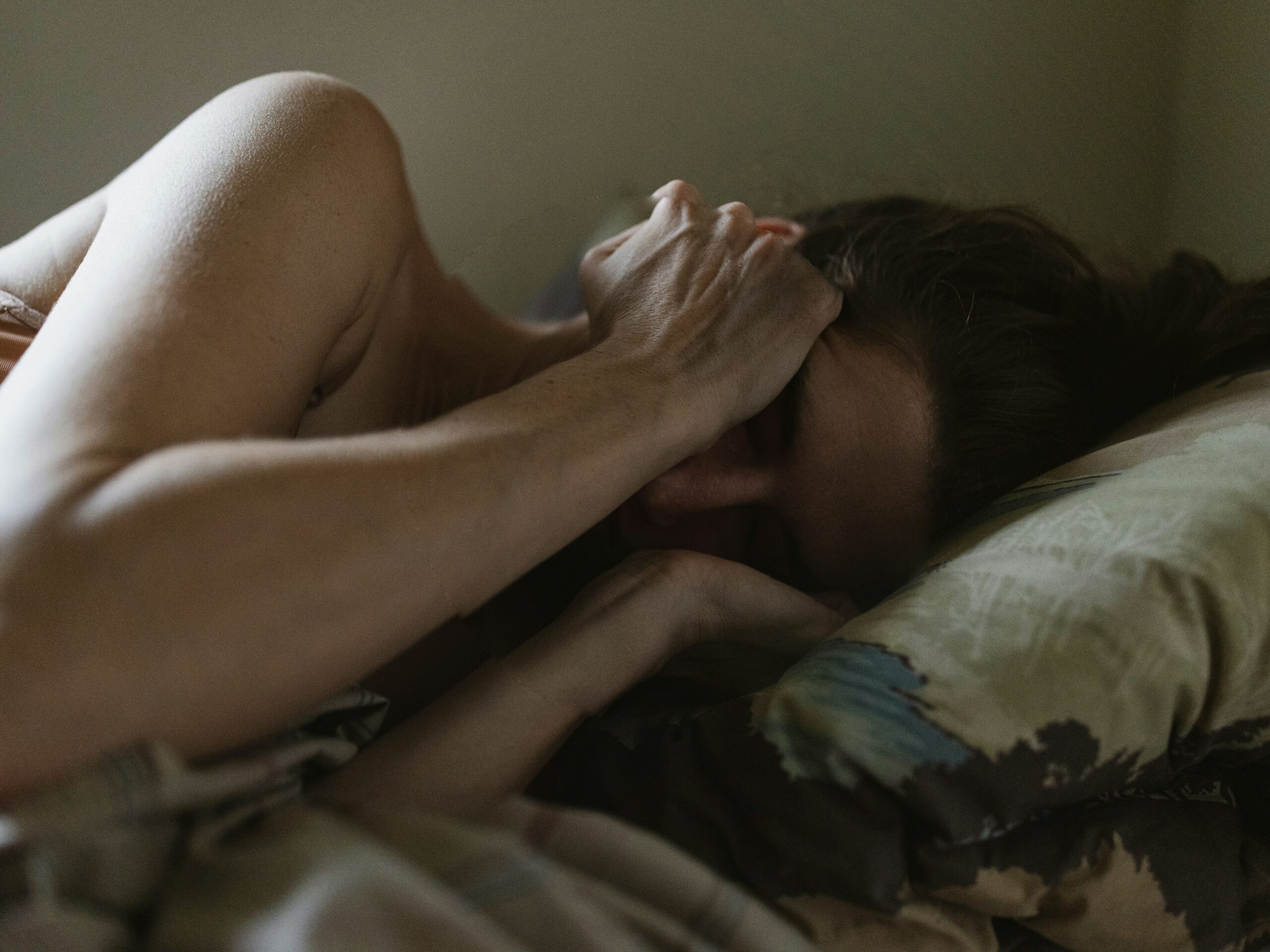 A woman lying in bed with her hands covering her face, appearing distressed. This image illustrates the emotional toll of abuse and the importance of domestic violence services for support and recovery.