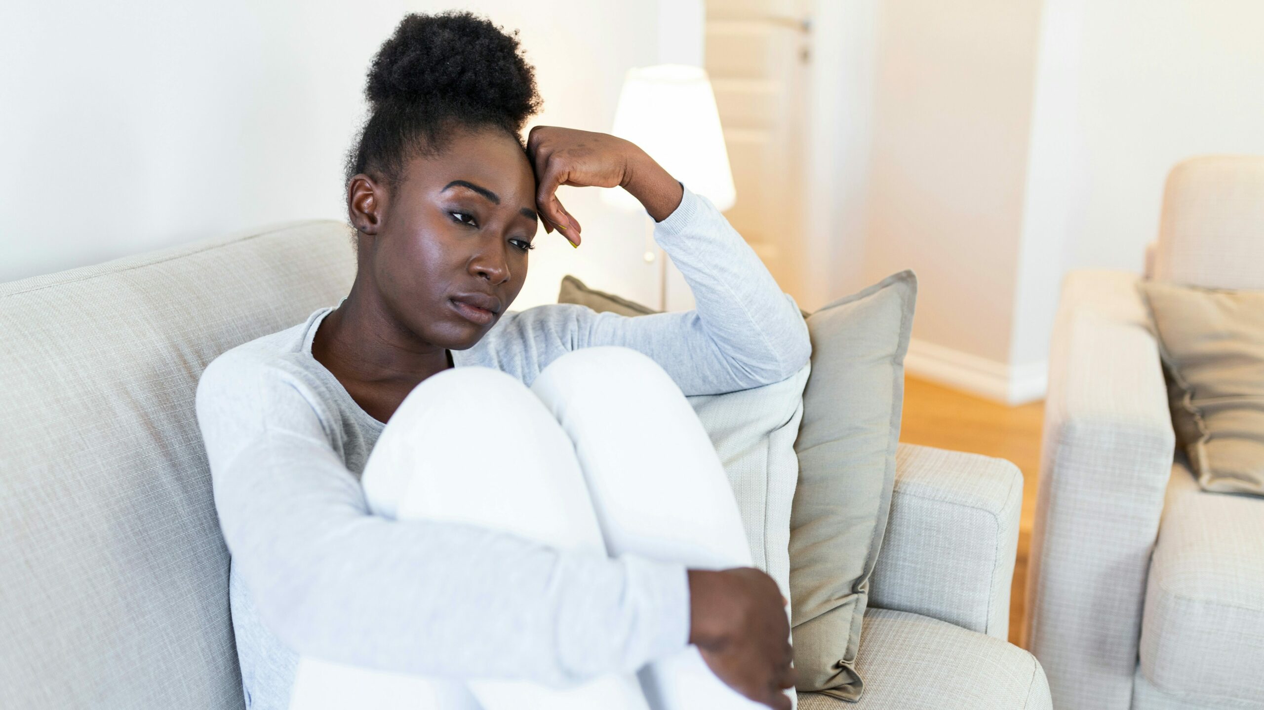 A woman sitting on a couch, hugging her knees and looking distressed. This image highlights the emotional impact of domestic abuse and the importance of accessible domestic violence services.