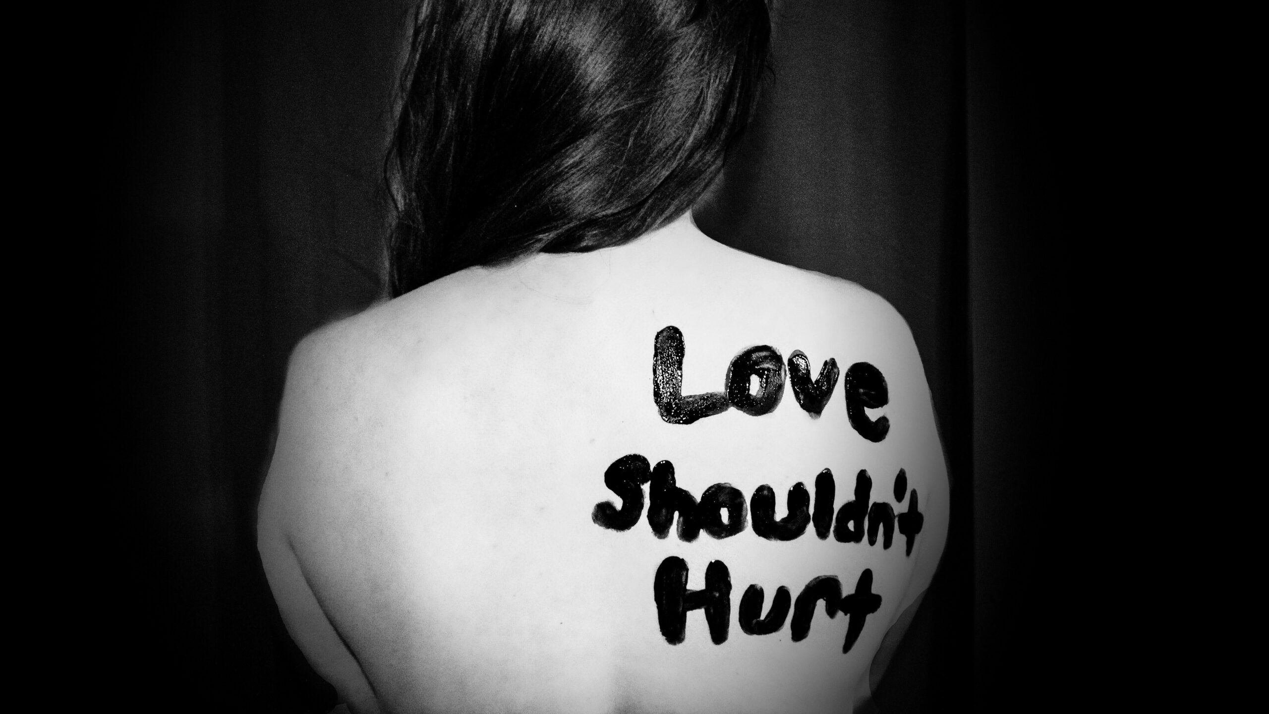 A woman with "Love Shouldn't Hurt" written on her back, highlighting the message against domestic abuse and the crucial need for domestic violence services.