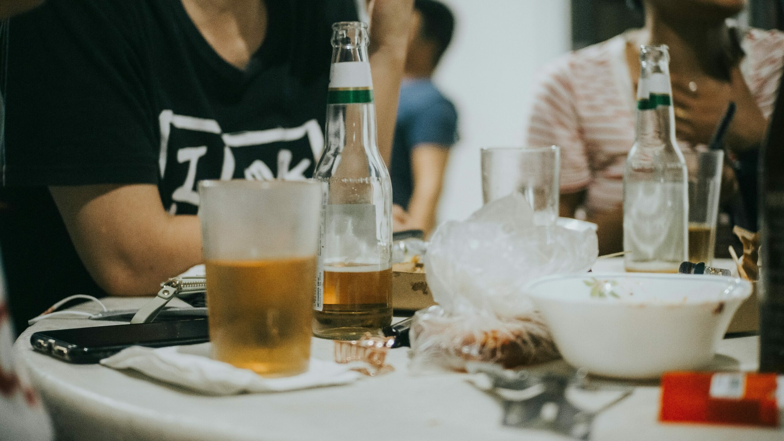 People sitting around a table with bottles of beer and glasses, engaged in conversation, suggesting summer substance use during a social gathering.