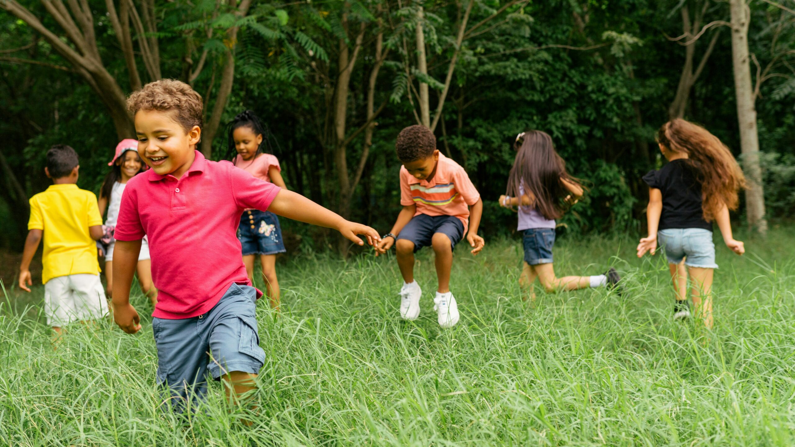 A group of children enjoying outdoor play, running and jumping in a grassy field, representing the positive impact of Children's Home and Community-Based Services (HCBS) on social skills and physical health.